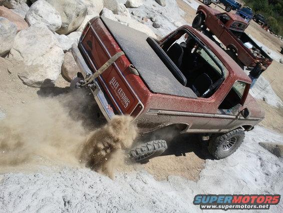1978 Ford Bronco climbing rocks, kicking up dust. Another Bronco is visible behind it