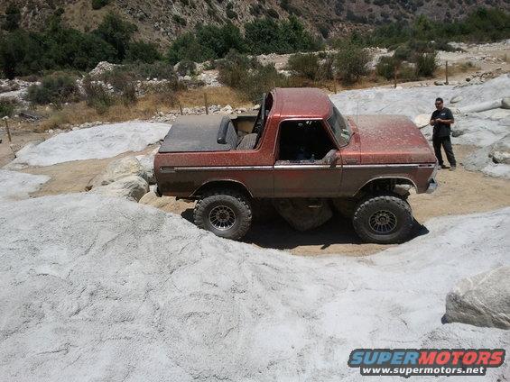 Red 1978 Ford Bronco navigating rocky terrain with a person standing nearby
