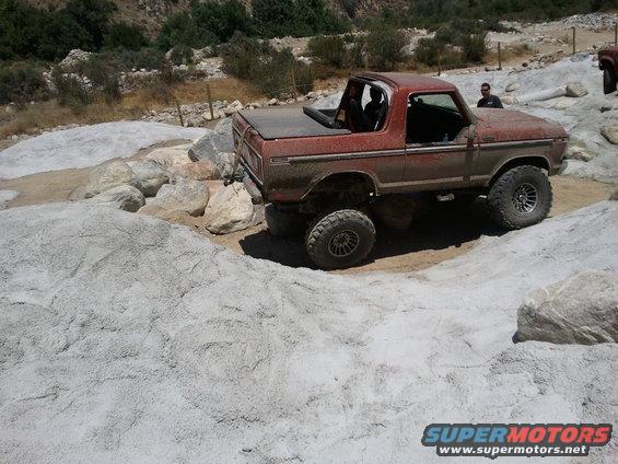 Red 1978 Ford Bronco on rocky terrain, side view, with a soft top