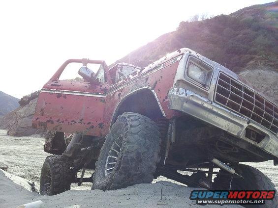 Red 1978 Ford Bronco with lifted suspension stuck in sand