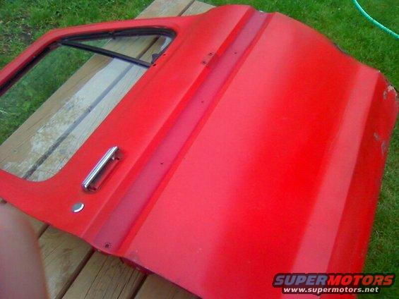 Red vehicle door with a chrome handle and a small vent window, resting on wooden planks