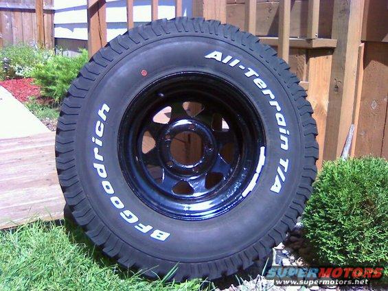 BFGoodrich All-Terrain T/A tire on a black rim, sitting on grass with a wooden fence in the background