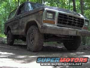 Mud-covered 1978 Ford Bronco in woods, front 3/4 view