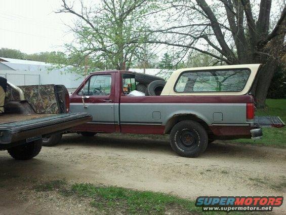 Ford pickup truck with a camper shell, carrying spare tires in the bed. The tailgate is down