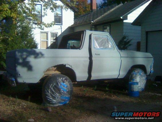 1979 Ford Bronco in primer with wheels covered, parked outside a house
