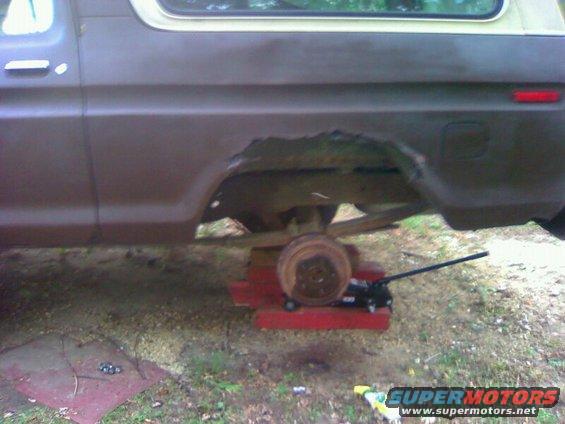 1979 Ford Bronco rear wheel well showing significant rust damage, supported by a jack and wooden blocks