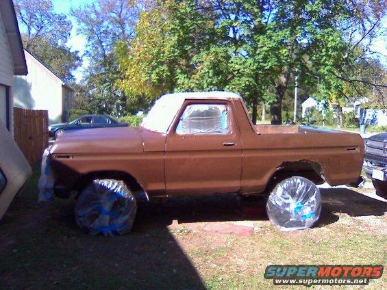 Brown Ford Bronco with windows taped off, parked outside with trees and a house in the background