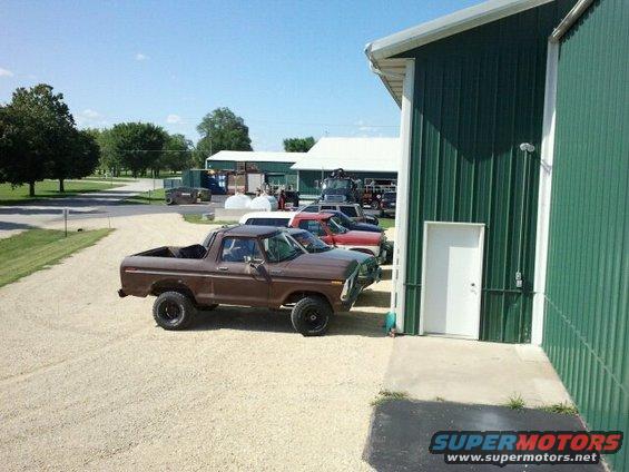 Brown pickup truck parked next to a green building, with other vehicles in the background