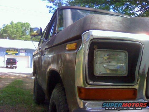 Brown 1978 Ford Bronco, front quarter view, showing rust and chrome grille. Another black SUV is visible in the background