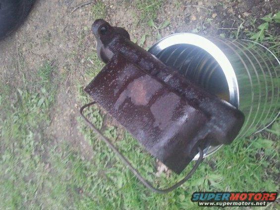 Rusty metal part with a wire handle inside a metal can on grass