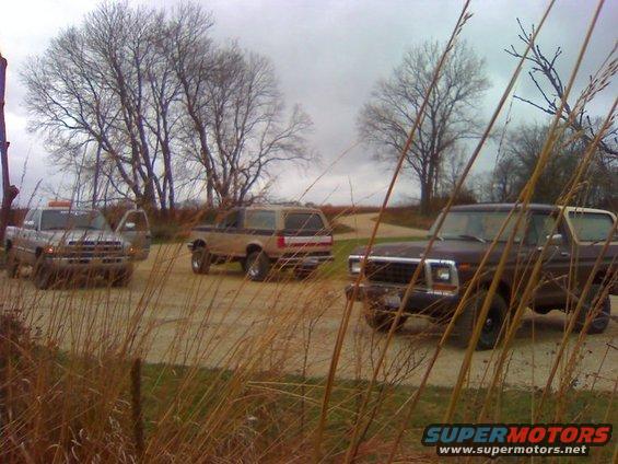 Three SUVs and a pickup truck parked on a dirt road with dry grass in the foreground