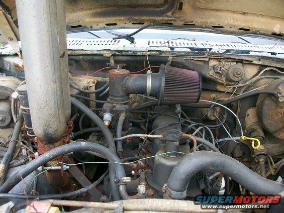 Engine bay with aftermarket air filter and large exhaust pipe. Rusty components visible
