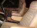 1984 Ford Bronco - The interior of a vehicle shows tan seats with plaid fabric inserts and vinyl armrests, along with a partial view of the steering wheel.
