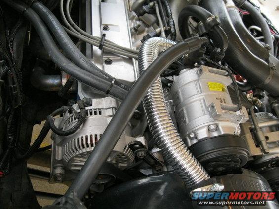 Close-up of engine bay parts including alternator, AC compressor, and hoses