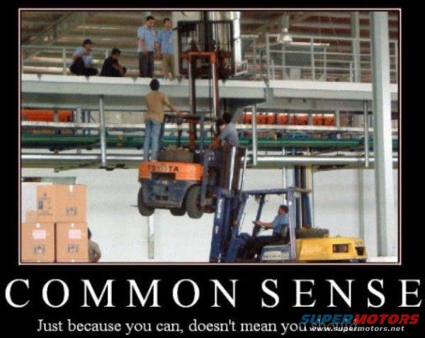 Two forklifts, one lifting the other, in a warehouse. People are watching from above
