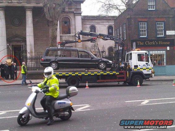 Hearse on tow truck, with a scooter in the foreground