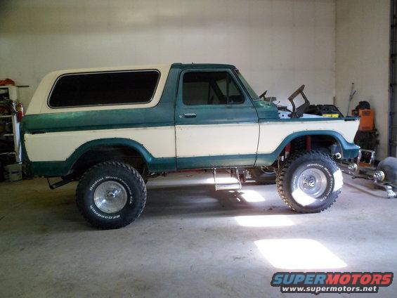 Two-tone green and white Ford Bronco lifted with off-road tires. Hood is open, showing the engine bay