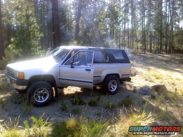 Silver SUV with a soft top, driver's door open, parked in a wooded area