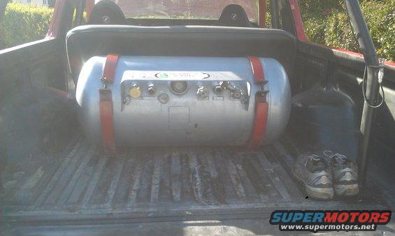 Propane tank with red straps in the bed of a red vehicle