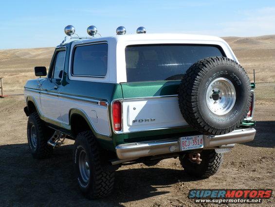 Green and white Ford Bronco with spare tire on back, parked on dirt road