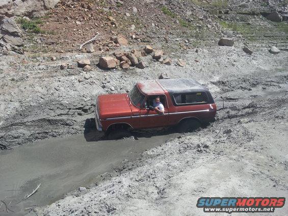 1978 Ford Bronco driving through a muddy rut on a rocky hillside