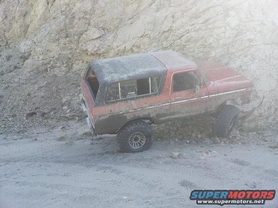 Red 1978 Ford Bronco on a dirt road next to a rocky incline