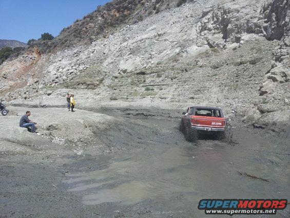Red 1978 Ford Bronco driving through mud, rear view