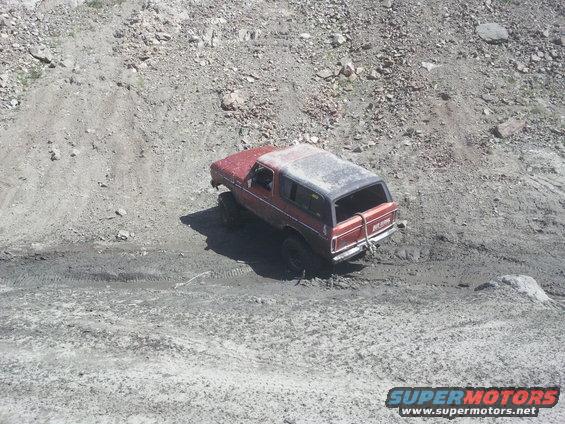 Red SUV with a black top is driving up a muddy, rocky incline