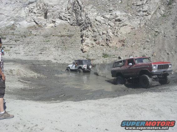 Red Ford Bronco and white Jeep Wrangler off-roading in mud pit