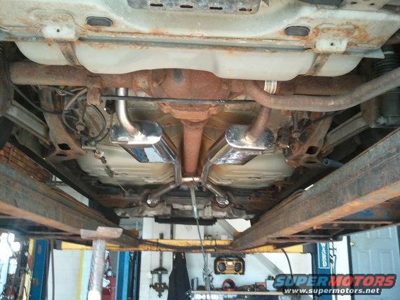 Underside of a car on a lift, showing the exhaust system and fuel tank