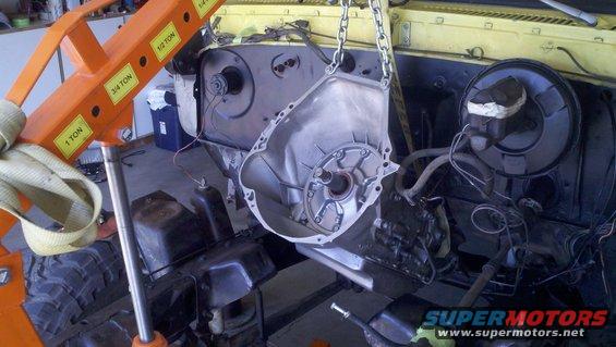 Orange engine hoist lifting a transmission housing from a yellow vehicle's engine bay