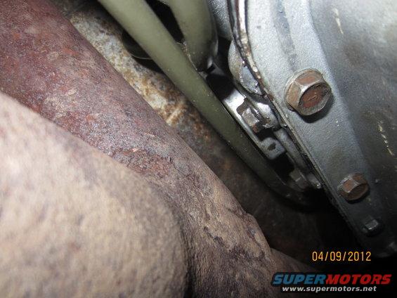 Close-up of rusty exhaust pipe and part of a transmission housing with bolts and lines