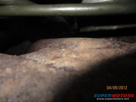 Rusty exhaust pipe and green metal frame under a vehicle