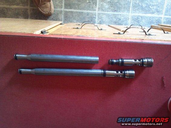 Metal valve parts on a red surface. Includes two long rods and two smaller valve bodies