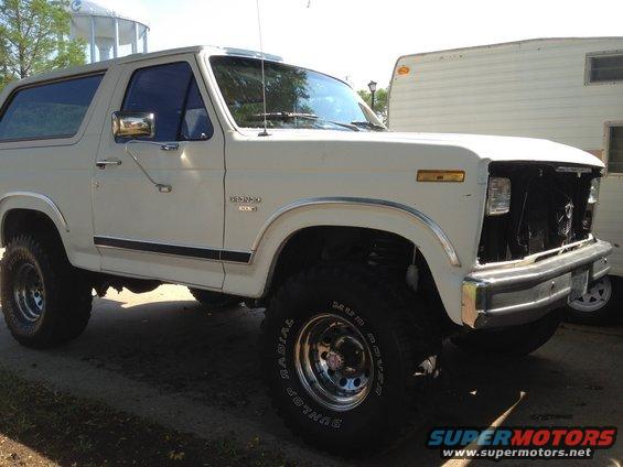 White Ford Bronco with aftermarket wheels and tires, parked next to a trailer