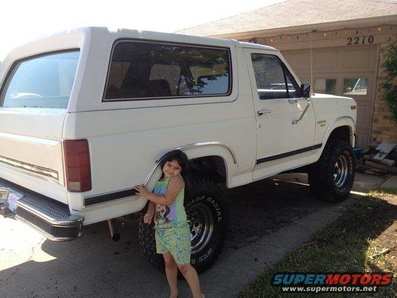 White 1984 Ford Bronco, rear 3/4 view, with a girl posing beside it