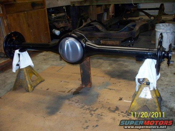Rear axle assembly on jack stands, with a partial frame and engine in the background