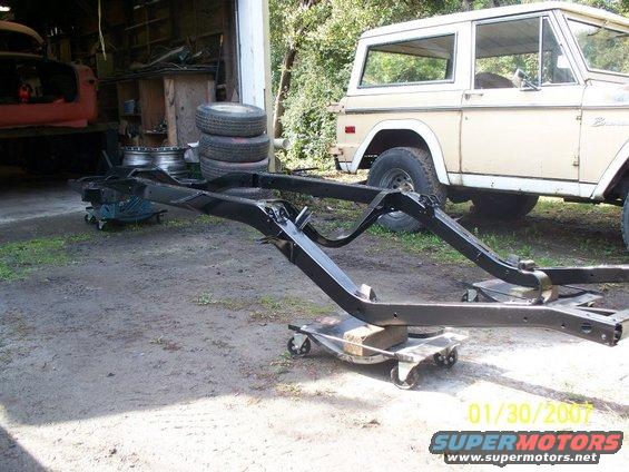 Tan 1978 Ford Bronco parked behind a black frame on dollies