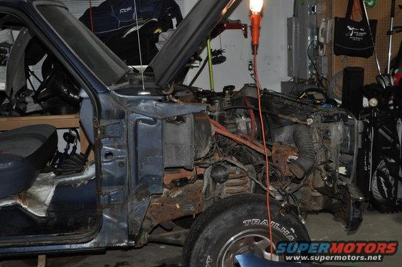 Blue Ford Bronco with hood open, showing disassembled engine and rusted frame