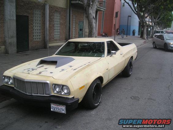 Cream 1975 Ford Ranchero with a grey hood scoop parked on a city street