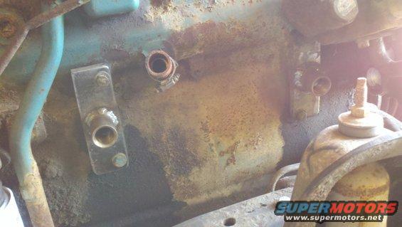 Engine bay showing metal brackets, hoses, and fittings on a rusty surface