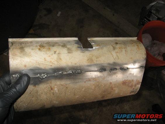 Someone is holding a section of exhaust pipe that has been cut and welded