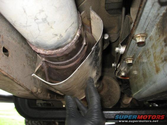 Exhaust pipe heat shield being held by a gloved hand, showing metal shielding and bolts
