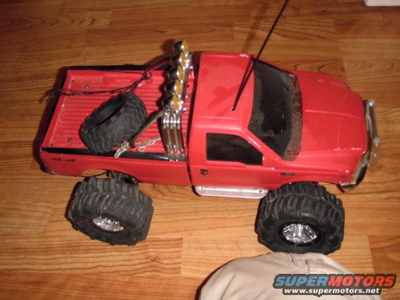 Red RC monster truck with large tires, dual exhaust stacks, and a spare tire in the bed
