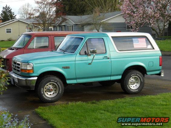 Teal Ford Bronco parked next to a red van. American flag sticker on rear window