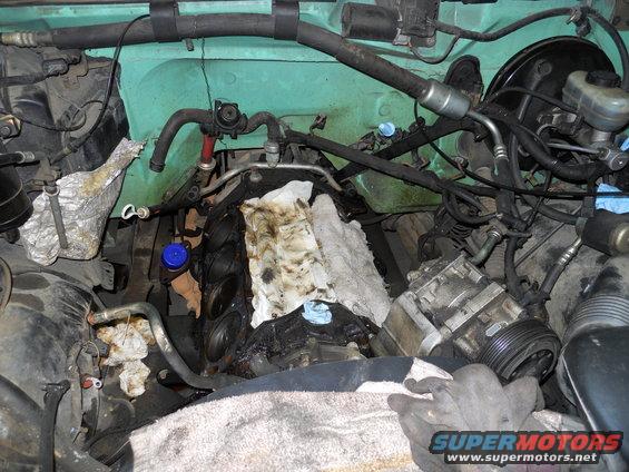 Engine bay with teal paint, showing engine components, hoses, and rags. A SuperMotors logo is visible