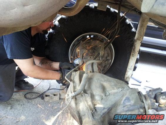 Man grinding on rear axle of a vehicle, sparks flying. Large tire visible