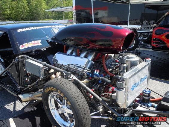 Black drag car engine with red flame graphics on the hood scoop, chrome intake, and a Ron Davis radiator