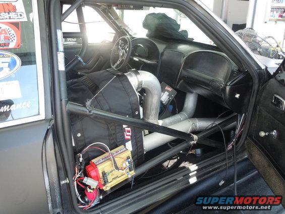 Car interior with roll cage, custom exhaust pipes, and racing seat. A yellow MSD ignition box is visible