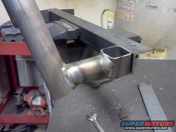 Welded metal pipe section held in a vise, with a square tube attached